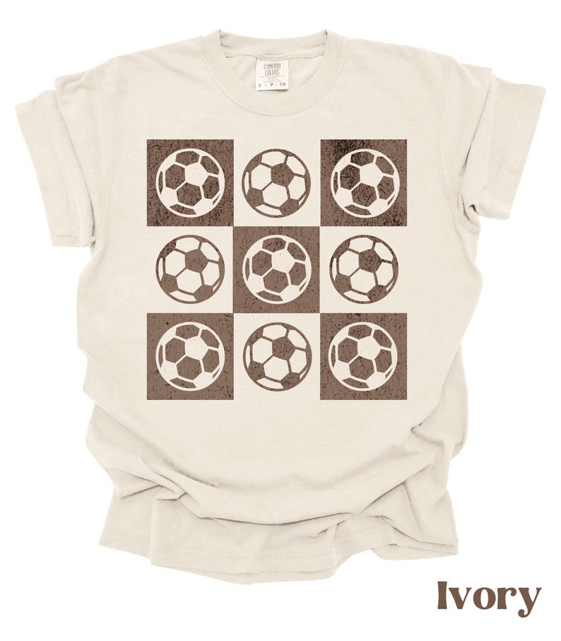 May include: Ivory t-shirt with a brown graphic of nine soccer balls arranged in a grid pattern.