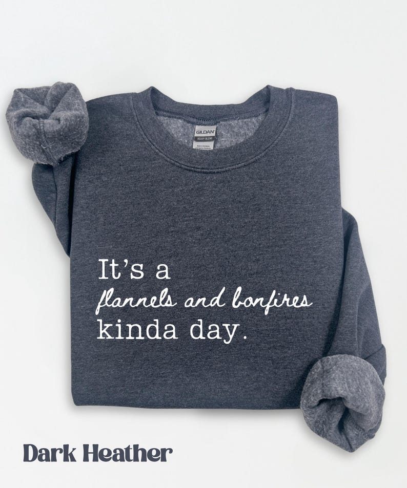 Puede incluir: Sudadera gris oscuro con el texto blanco "It's a flannels and bonfires kinda day". Las mangas est&aacute;n dobladas. La sudadera es de la marca Gildan.