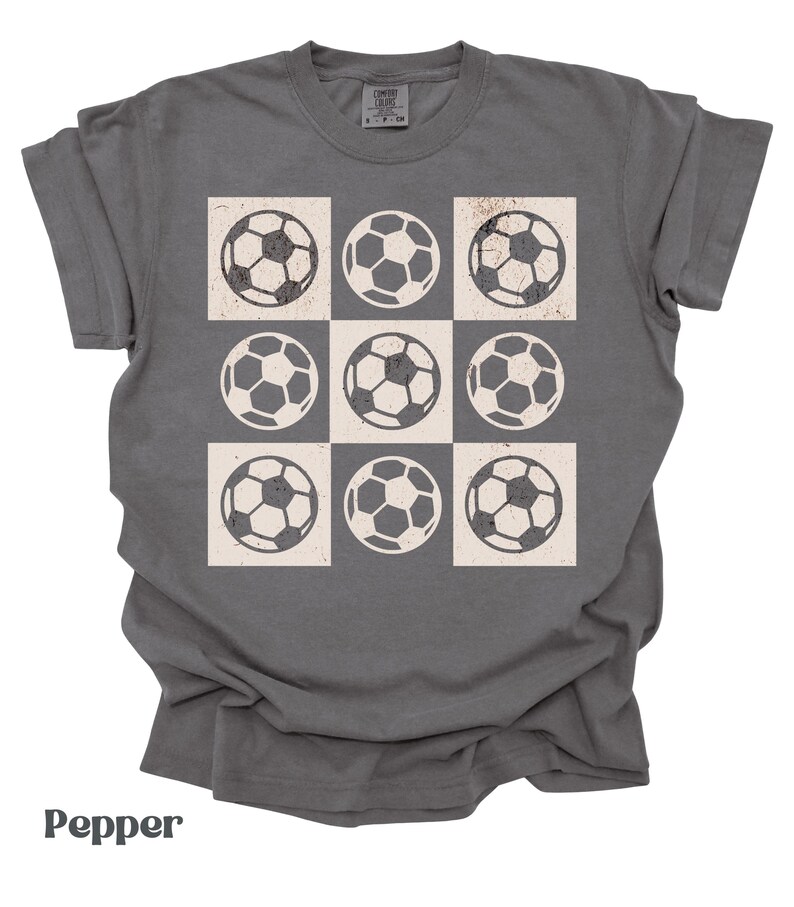 May include: A dark gray t-shirt with a white checkered pattern featuring nine soccer balls.