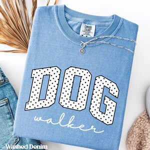 Könnte beinhalten: Hellblaues "Comfort Colors" T-Shirt mit dem Wort "DOG" in großen, schwarz umrandeten Buchstaben, die mit weißen Punkten gefüllt sind. Darunter steht das Wort "walker" in Schreibschrift. Eine silberne Halskette mit Anhänger befindet sich auf dem Shirt.