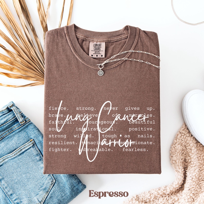 May include: A brown t-shirt with the words "Lung Cancer Warrior" defined as "fierce, strong, never gives up, believe of miracles, brave, courageous, beautiful, faithful, inspirational, positive, strong willed, tough as nails, resilient, tenacious, passionate, fighter, unbreakable, fearless".
