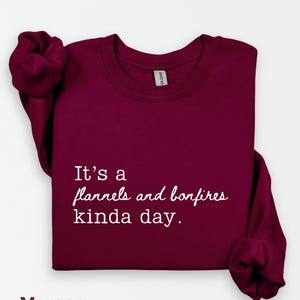 Puede incluir: Sudadera burdeos con cuello redondo con el texto "It's a flannels and bonfires kinda day." La sudadera es de color burdeos liso. Las mangas est&aacute;n dobladas. La palabra "Maroon" est&aacute; en la parte inferior de la imagen.