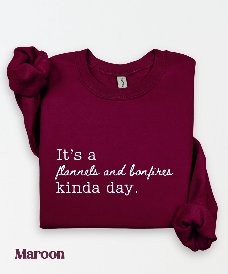 Puede incluir: Sudadera burdeos con cuello redondo con el texto "It's a flannels and bonfires kinda day." La sudadera es de color burdeos liso. Las mangas est&aacute;n dobladas. La palabra "Maroon" est&aacute; en la parte inferior de la imagen.