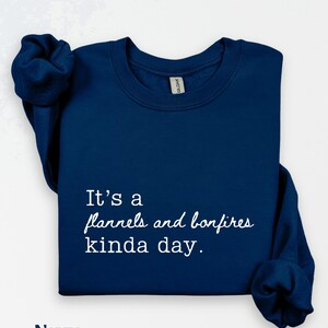 Puede incluir: Sudadera azul marino con el texto "It's a flannels and bonfires kinda day." La palabra "Navy" est&aacute; impresa en la parte inferior. La sudadera tiene mangas largas.