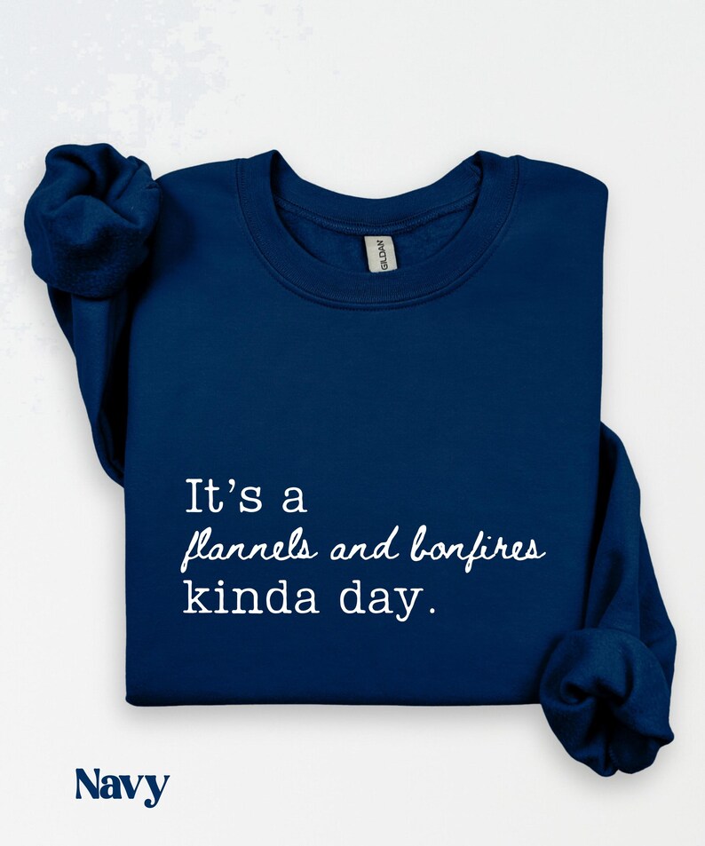 Puede incluir: Sudadera azul marino con el texto "It's a flannels and bonfires kinda day." La palabra "Navy" est&aacute; impresa en la parte inferior. La sudadera tiene mangas largas.