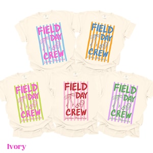 May include: Ivory-colored t-shirts with the words "FIELD DAY CREW" in various colors, including blue, orange, pink, green, and purple. The text is set against a striped background. The words "Jackson Elementary" are also printed on the shirts.