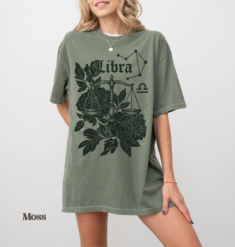 Op de afbeelding: Een mosgroen t-shirt met een Weegschaal sterrenbeeld ontwerp. De afbeelding bevat het woord "Libra", een weegschaal, bloemmotieven en het Weegschaal sterrenbeeld. Het t-shirt heeft een relaxte pasvorm.