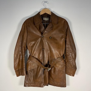 May include: A brown leather jacket with a belt and double breasted closure.