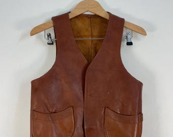 May include: A brown leather vest with two large pockets on the front. The vest has a V-neck and is made of a soft, supple leather.