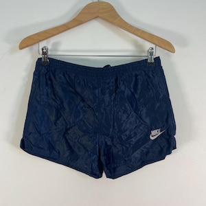 May include: Navy blue nylon athletic shorts with a white Nike logo on the right leg.