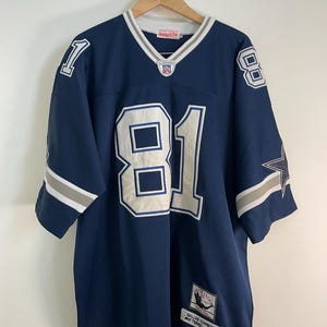 Puede incluir: Una camiseta de fútbol azul marino con el número 81 en blanco, contorneado en azul. La camiseta tiene rayas blancas y grises en las mangas y el cuello. Un parche de los Dallas Cowboys es visible en la parte inferior derecha.