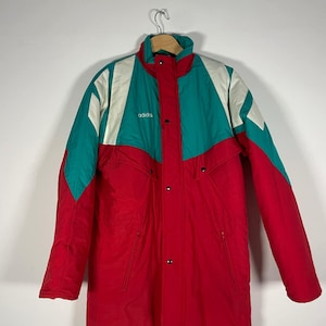 Könnte beinhalten: Eine vintage Adidas Skijacke in Rot, Weiß und Tealblau mit Reißverschluss und Knopfleiste. Die Jacke hat einen hohen Kragen und einen Kordelzug in der Taille.