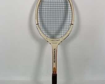 Könnte beinhalten: Ein weißer und brauner Tennisschläger mit einem blauen Besaitungskopf. Der Schläger trägt den Text "LADY PRO" und "TOURNAMENT". Der Markenname "ROSSIGNOL" ist auf dem Griff aufgedruckt.