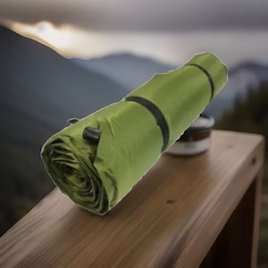 Peut inclure: Un matelas de camping vert roulé et sécurisé avec une sangle noire. Le matelas est sur une surface en bois.