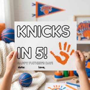 Op de afbeelding: Een witte rechthoekige kaart met de zwart omlijnde tekst KNICKS IN 5! en de tekst HAPPY FATHER'S DAY! met lege regels voor datum en ondertekening. Een oranje handafdruk bevindt zich rechts van de tekst op de kaart.