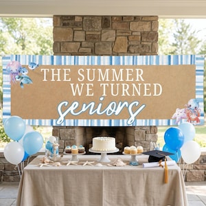 Può includere: Un banner con la scritta "THE SUMMER WE TURNED seniors" è esposto sopra un tavolo allestito per una festa di laurea. Lo striscione ha uno sfondo marrone con strisce blu e bianche. Il tavolo è decorato con palloncini, una torta, cupcake e conchiglie.