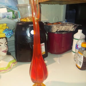 May include: A tall, orange glass vase with a flared, yellow base. The vase has a unique, wavy design and is perfect for displaying flowers.
