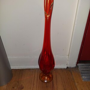 May include: A tall, red glass vase with a flared opening and a rounded base. The vase has a yellow-gold tint at the top and bottom.