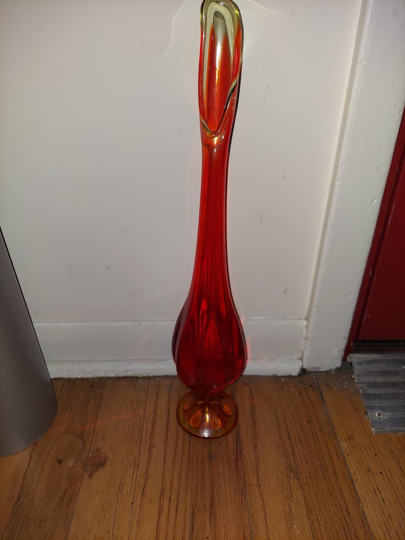 May include: A tall, red glass vase with a flared opening and a rounded base. The vase has a yellow-gold tint at the top and bottom.
