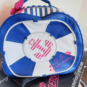 May include: A blue and white striped nautical themed bag with a pink bow, anchor, and the text "S.S. Betsey Johnson".