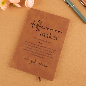 May include: Brown leather journal with the words "difference maker" and the definition of the word. The definition includes the phonetic spelling of the word. The journal also has the word "Archer" written on it.