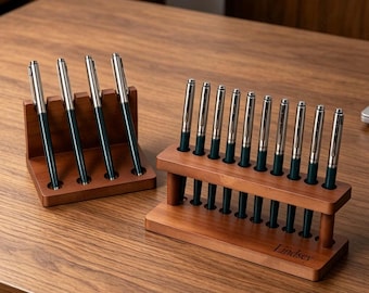 May include: Two wooden pen display stands with a dark brown finish. One stand holds four pens in a single row, while the larger stand holds ten pens in a single row. The larger stand features the name Lindsey engraved on the front wooden base.