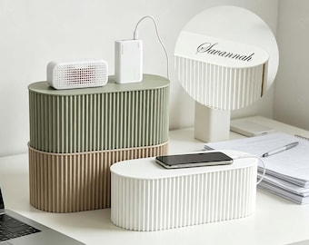 Op de afbeelding: Drie kabel organizers in groen, beige en wit, met een geribbeld ontwerp. Een telefoon ligt op de witte doos en een powerbank en luidspreker staan bovenop de groene doos. De naam "Savannah" staat op de witte doos.