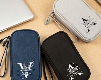 May include: Three rectangular zippered pouches in navy blue, black, and light gray. Each pouch features a personalized name printed in white or black ink, integrated into a decorative letter design with floral accents and a wrist strap.