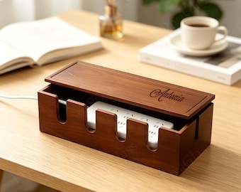 May include: A rectangular dark wood cable management box with a removable lid featuring the engraved name Antonia. The box has four U-shaped cutouts along the front edge for cords and contains a white power strip with multiple electrical outlets.