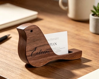 May include: A dark brown wooden bird-shaped business card holder with a smooth finish. The side of the bird features the name Eileen engraved in a black cursive script. A white business card is inserted into the slot on the bird's back.