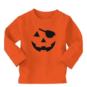 Può includere: Maglietta arancione a maniche lunghe con un disegno di zucca nera. Il design include una benda sull'occhio nera, occhi triangolari e una bocca ampia e sorridente. La maglietta è in materiale morbido, perfetta per Halloween.