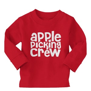 Puede incluir: Camiseta roja de manga larga con texto blanco que dice "apple picking crew" con un pequeño gráfico de manzana.
