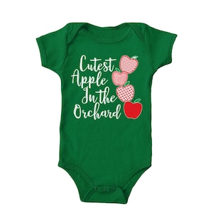 May include: A green baby onesie with the text "Cutest Apple in the Orchard" and a stack of red apples with white designs.