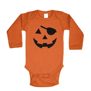 May include: Orange baby bodysuit with long sleeves. The front features a black jack-o'-lantern face with an eye patch. The bodysuit has a snap closure at the bottom. Ideal for Halloween.
