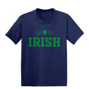 Puede incluir: Una camiseta azul marino con un trébol verde y el texto "Wee Bit Irish" en verde.