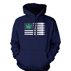 May include: Navy blue hooded sweatshirt featuring a graphic of the American flag with a green cannabis leaf in the corner and white joints replacing the stripes. The sweatshirt has a front pocket and a drawstring hood.
