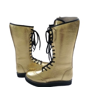 May include: A pair of gold wrestling boots with black laces. The boots are tall and have a thick sole.