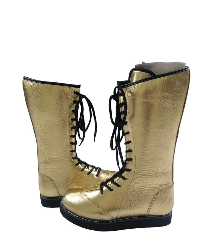 May include: A pair of gold wrestling boots with black laces. The boots are tall and have a thick sole.