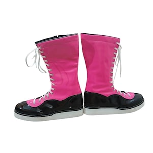 Könnte beinhalten: Paar kniehohe Stiefel in Pink und Schwarz mit weißen Schnürsenkeln. Die Stiefel haben eine glänzende Oberfläche auf dem rosafarbenen Oberteil und dem schwarzen Unterteil. Die Sohlen sind weiß und die Stiefel sind für einen festen Sitz konzipiert.