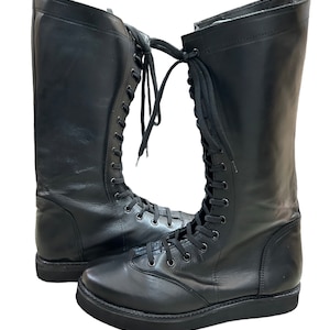 Puede incluir: Un par de botas de lucha libre de cuero negro con cordones. Las botas tienen una suela gruesa y son de altura de rodilla.