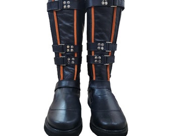 Puede incluir: Un par de botas de cuero negro con costuras naranjas y múltiples hebillas. Las botas tienen una punta puntiaguda y un tacón grueso.