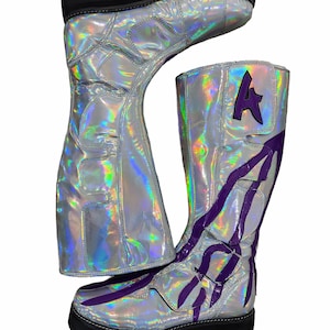 Könnte beinhalten: Silberne, holografische kniehohe Stiefel mit schwarzer Sohle und lila Akzenten. Die Stiefel haben eine Plateausohle und ein lila "A" an der Seite. Das Design umfasst lila blitzartige Muster.