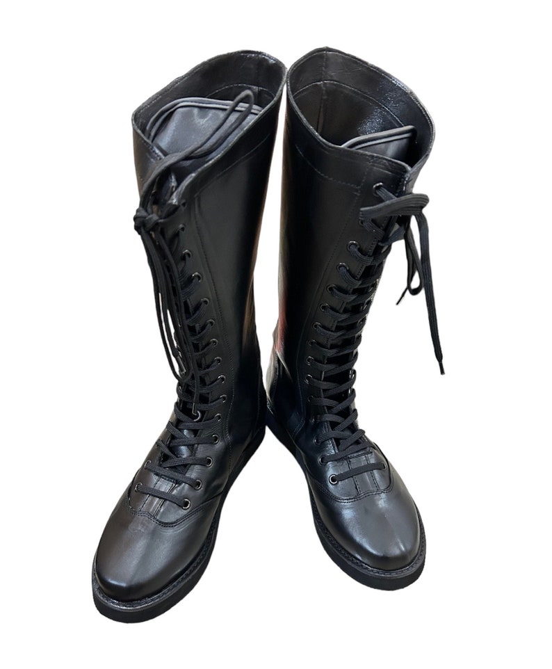 Puede incluir: Un par de botas negras de cuero hasta la rodilla con cierre de cordones. Las botas tienen una punta redonda y una suela gruesa.