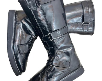 Puede incluir: Par de botas negras brillantes hasta la rodilla con múltiples correas con hebillas y una suela gruesa negra. Las botas tienen un aspecto de charol brillante y están diseñadas con una punta redonda. Las costuras blancas acentúan la suela.