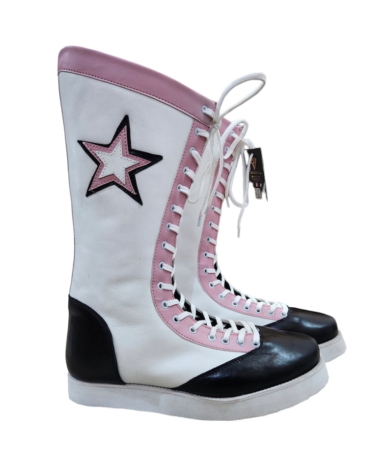 May include: White leather wrestling boots with black leather accents and pink trim. The boots have a star design on the side and white laces.