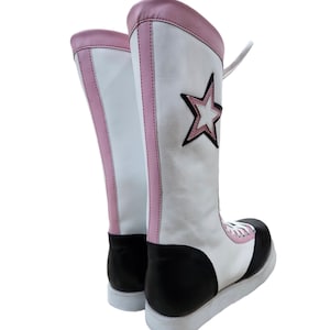 May include: A pair of white wrestling boots with pink trim and a black star on the side. The boots have black soles and white laces.