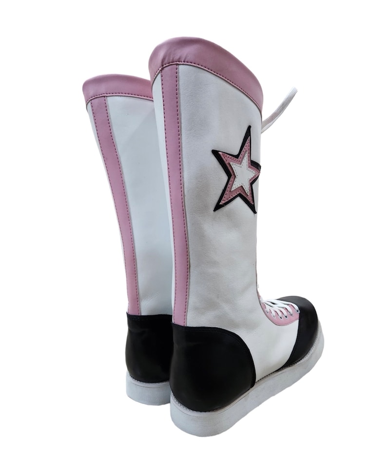 May include: A pair of white wrestling boots with pink trim and a black star on the side. The boots have black soles and white laces.