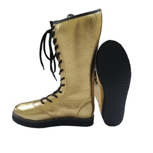 May include: A pair of gold wrestling boots with black laces and a black rubber sole.