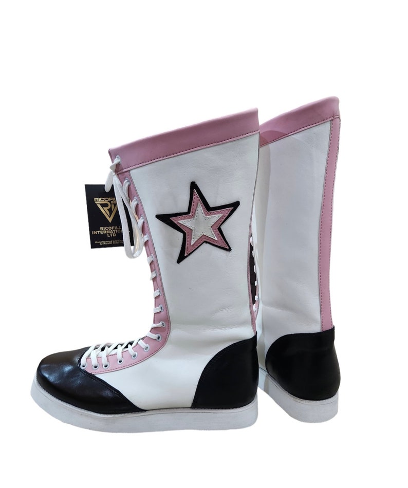 May include: White wrestling boots with black and pink accents. The boots have a star design on the side and are laced up the front. The boots are made by Riccoflex International LTD.