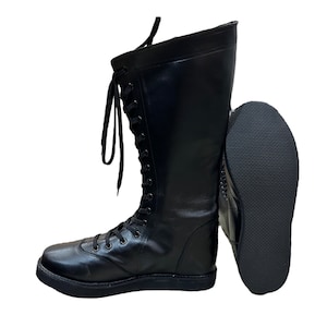 Puede incluir: Botas de lucha libre de cuero negro con cordones en el lateral y suela gruesa. Las botas se muestran con la suela de una bota mirando hacia la c&aacute;mara.